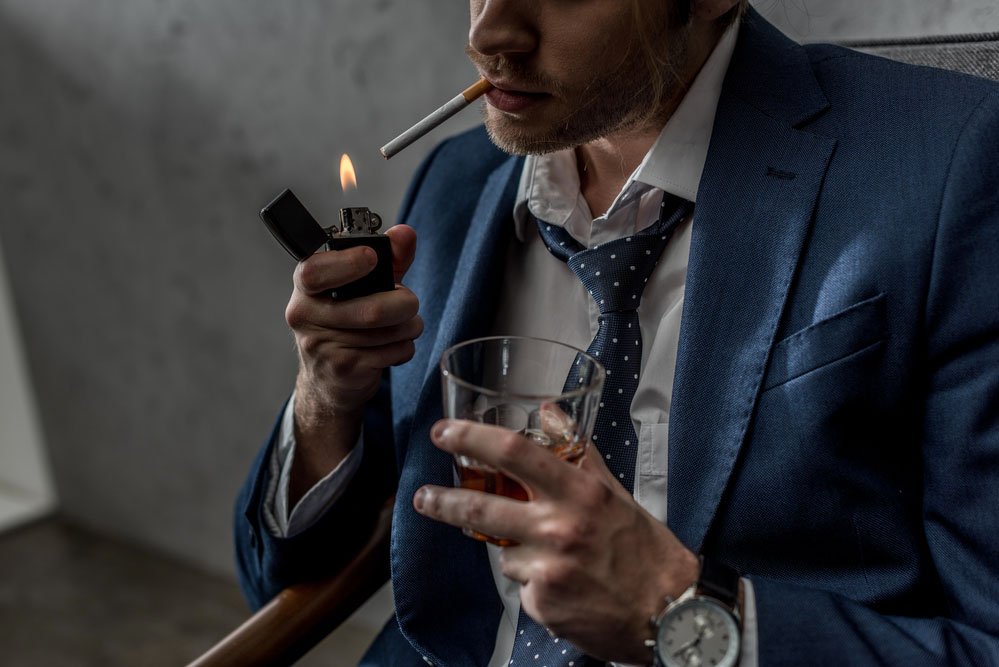 Man lighting a cigarette while drinking an alcoholic beverage